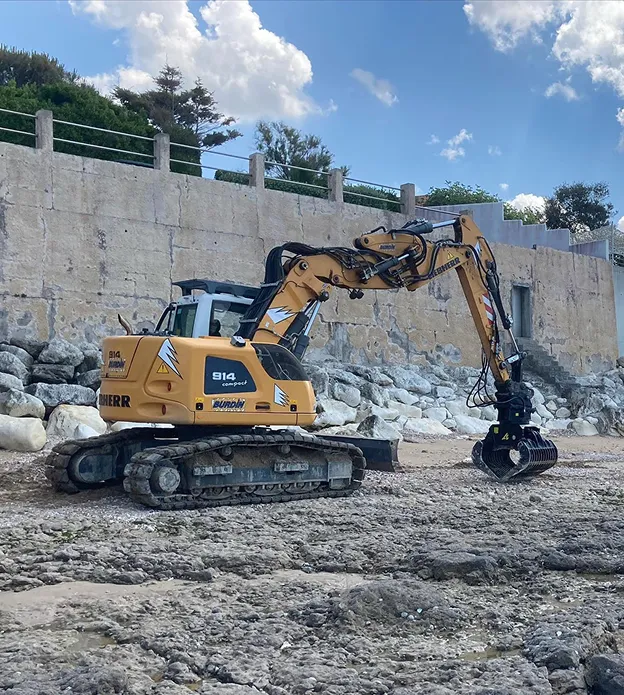 Pelle Liebherr 914 compacte jaune sur une plage rocheuse, travaillant près d'un mur à Corme-Royal en Charente-Maritime 17