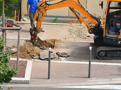 Une pelleteuse creuse un trou sur le trottoir, un homme à côté à Corme-Royal en Charente-Maritime 17