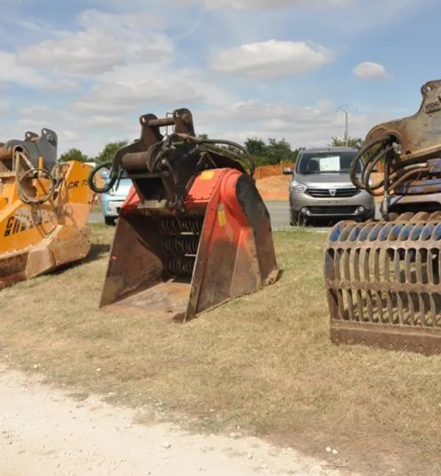 Plusieurs godets de pelle mécanique et accessoires d'équipement lourd exposés en plein air à Corme-Royal en Charente-Maritime 17